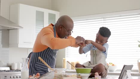 Happy-african-american-grandfather-and-grandson-having-fun,-baking-in-kitchen,-slow-motion