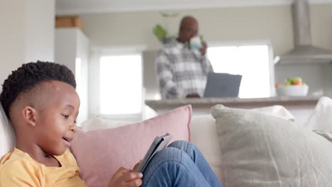African-american-grandfather-with-grandson-using-tablet-on-couch-at-home,-slow-motion