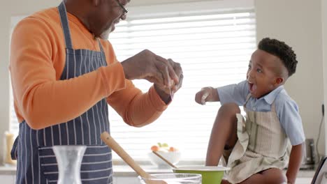 Happy-african-american-grandfather-and-grandson-having-fun,-baking-in-kitchen,-slow-motion