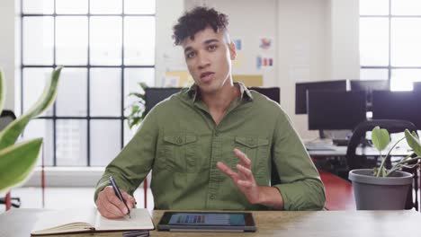 Portrait-of-biracial-male-designer-in-video-call-at-computer-in-casual-office,-slow-motion