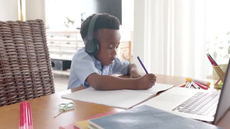 Happy-african-american-boy-in-headphones-drawing,-using-laptop-for-online-class-at-home,-slow-motion