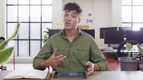 Portrait-of-biracial-male-designer-in-video-call-at-computer-in-casual-office,-slow-motion