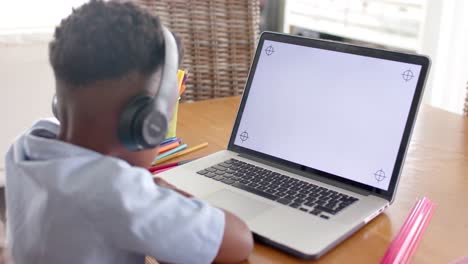 African-american-boy-in-headphones-using-laptop-in-online-class-at-home,-slow-motion,-copy-space