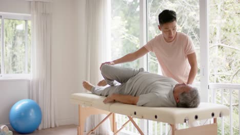 Diverse-male-physiotherapist-advising-and-senior-male-patient-stretching,-in-slow-motion
