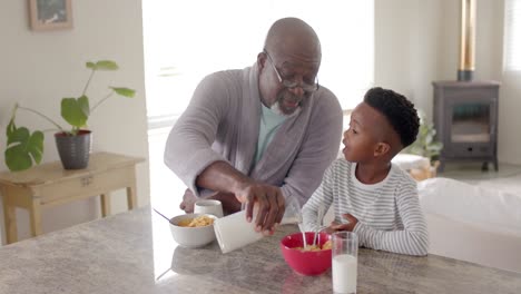 Happy-african-american-grandfather-having-breakfast-with-grandson-in-kitchen,-slow-motion