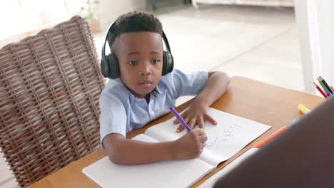 Fröhlicher-Afroamerikanischer-Junge-Mit-Kopfhörern,-Der-Zu-Hause-Einen-Laptop-Für-Den-Online-Unterricht-Benutzt,-Zeitlupe