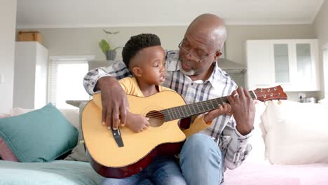 Happy-african-american-grandfather-and-grandson-playing-guitar-together-at-home,-slow-motion