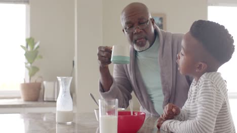 Glücklicher-Afroamerikanischer-Großvater-Beim-Frühstück-Im-Gespräch-Mit-Enkel-In-Der-Küche,-Zeitlupe