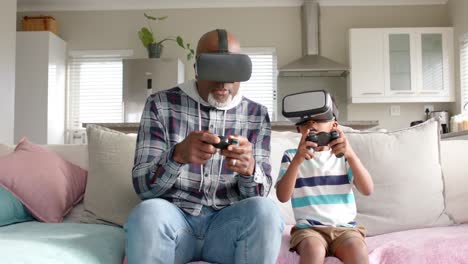 African-american-grandfather-and-grandson-sitting-on-sofa,-having-fun,-using-vr-headset,-slow-motion