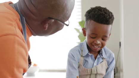 Happy-african-american-grandfather-and-grandson-talking,-baking-in-kitchen,-slow-motion