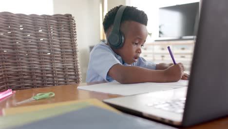 Fröhlicher-Afroamerikanischer-Junge-Mit-Kopfhörern,-Der-Zu-Hause-Einen-Laptop-Für-Den-Online-Unterricht-Benutzt,-Zeitlupe