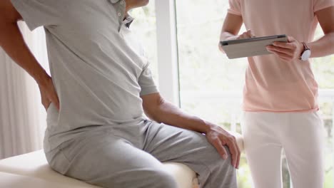 Diverse-male-physiotherapist-with-tablet-examinig-senior-male-patient,-in-slow-motion