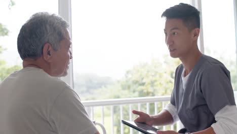 Diverse-male-doctor-with-tablet-discussing-with-senior-male-patient-at-home,-slow-motion