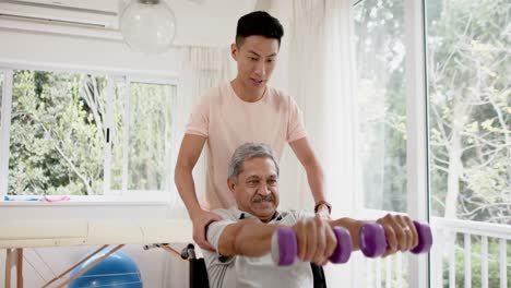 Verschiedene-Männliche-Physiotherapeuten-Beraten-Und-älterer-Mann-Im-Rollstuhl-Mit-Hanteln,-In-Zeitlupe