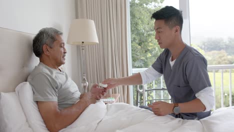 Diverse-male-doctor-and-senior-male-patient-discussing-in-bed-at-home,-slow-motion