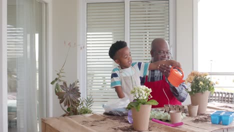 Happy-african-american-grandfather-and-grandson-watering-flowers-on-balcony,-slow-motion