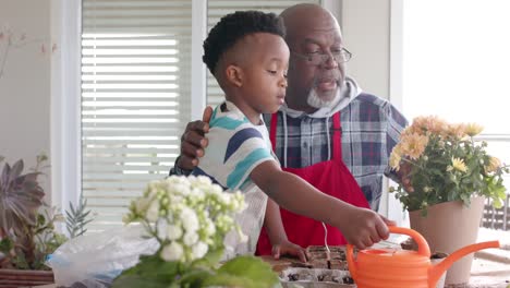 African-american-grandfather-and-grandson-embracing,-watering-flowers-on-balcony,-slow-motion