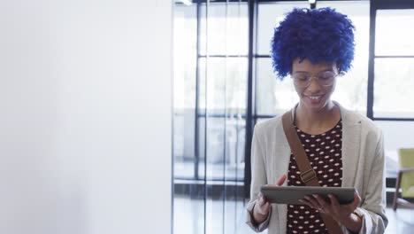 Happy-biracial-businesswoman-with-blue-afro-using-tablet-in-office,-copy-space,-slow-motion