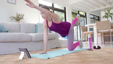 Focused-caucasian-woman-exercising-at-home-on-mat-with-tablet-in-slow-motion