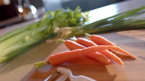 Verduras-Orgánicas-Y-Pelador-Sobre-Encimera-En-Cocina-Soleada,-Cámara-Lenta