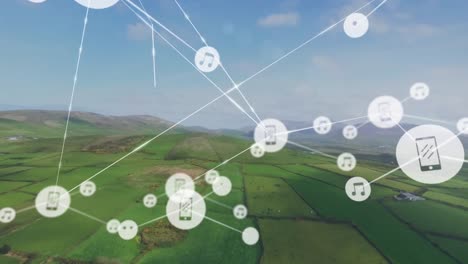 Animation-of-connected-icons-over-aerial-view-of-green-field-against-mountains-and-cloudy-sky