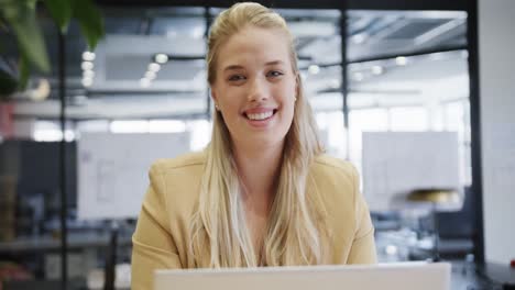 Portrait-of-happy-plus-size-caucasian-casual-businesswoman-using-laptop-at-desk