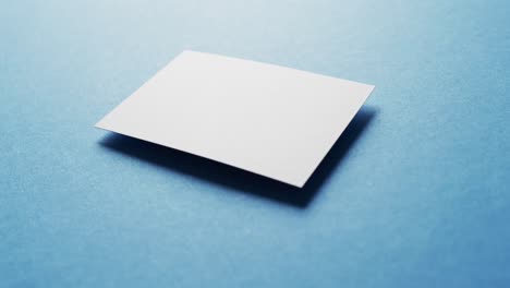 Blank-white-business-card-on-blue-background,-copy-space,-slow-motion
