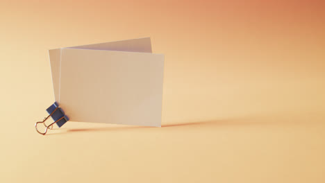Zwei-Leere-Weiße-Visitenkarten-Mit-Bulldoggen-Clip-Auf-Orangefarbenem-Hintergrund,-Kopierraum,-Zeitlupe