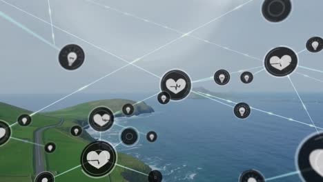 Animation-of-connected-icons-over-aerial-view-of-road-on-mountain-with-sea-against-cloudy-sky