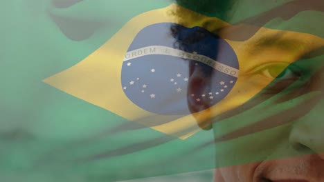 Animation-of-flag-of-brazil-over-cropped-close-up-portrait-of-biracial-man-standing-at-beach