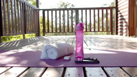 Towel,-bottle-of-water,-earphones-and-smartphone-on-yoga-mat-at-log-cabin,-slow-motion