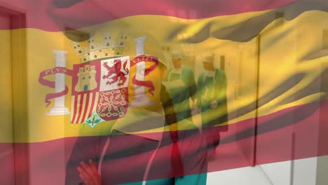 Animation-of-flag-of-spain,-biracial-female-surgeon-standing-arms-crossed-in-corridor-of-hospital