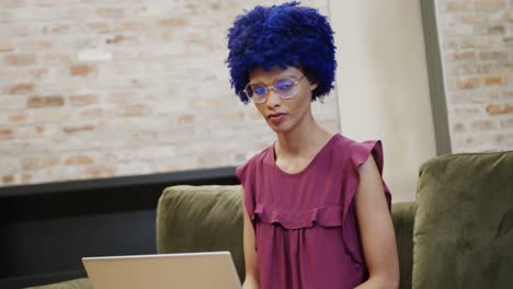 Portrait-of-happy-biracial-businesswoman-with-blue-afro-using-laptop,-slow-motion