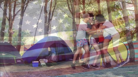 Animation-of-flag-of-america-waving,-happy-diverse-friends-hugging-and-jumping-near-camping-tents