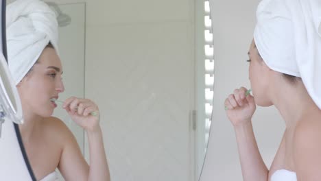 Caucasian-woman-with-towel-on-head-brushing-teeth-in-bathroom,-slow-motion
