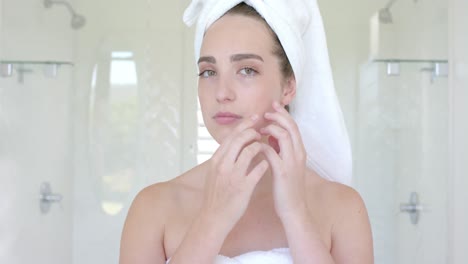 Portrait-of-caucasian-woman-with-towel-on-head-touching-her-face-in-bathroom-in-slow-motion