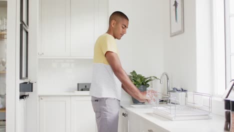 Biracial-man-washing-dishes-in-bright-kitchen,-slow-motion