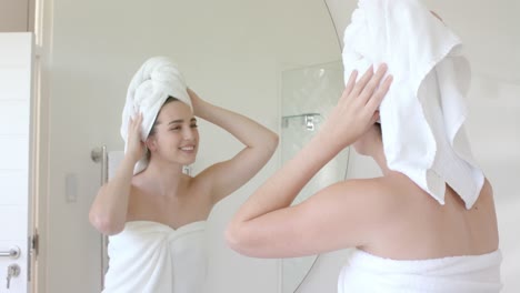 Happy-caucasian-woman-looking-in-front-of-mirror-with-towel-on-head-in-bathroom-in-slow-motion