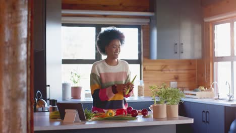 Glückliche-Afroamerikanische-Frau,-Die-In-Der-Sonnigen-Küche-Eine-Mahlzeit-Mit-Einem-Tablet-Zubereitet