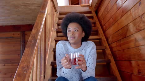 Happy-african-american-woman-drinking-tea-sitting-on-stairs,-in-slow-motion