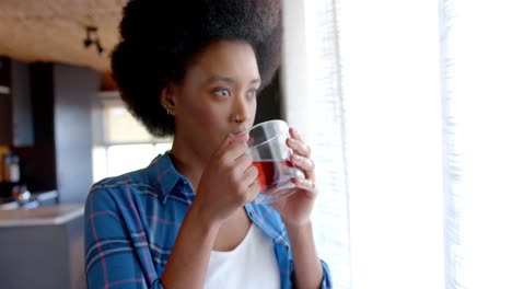 Mujer-Afroamericana-Bebiendo-Té-En-Una-Cocina-Soleada,-En-Cámara-Lenta
