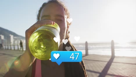 Animation-of-heart-icon-with-numbers-over-biracial-female-athlete-drinking-water-against-sea