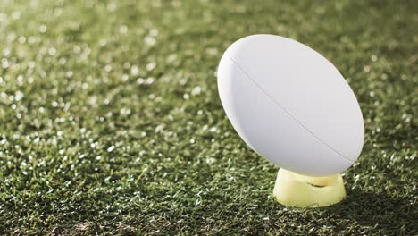 White-rugby-ball-on-kicking-tee-on-sunlit-grass-with-copy-space,-slow-motion