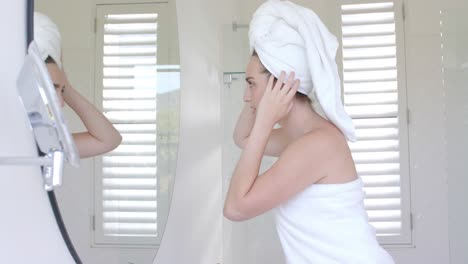 Happy-caucasian-woman-looking-in-front-of-mirror-with-towel-on-head-in-bathroom-in-slow-motion