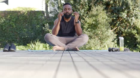 Focused-african-american-man-doing-yoga-meditation-on-deck-in-sunny-garden,-slow-motion