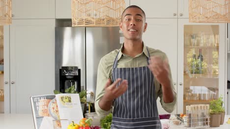 Biracial-male-cooking-vlogger-in-apron-talking-and-filming-in-kitchen