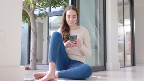 Happy-caucasian-woman-sitting-on-floor-and-using-smartphone-in-slow-motion