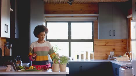 Happy-african-american-woman-preparing-meal-using-tablet-in-sunny-kitchen