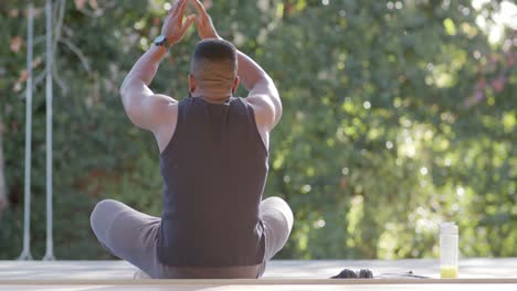 Hombre-Afroamericano-Enfocado-Haciendo-Meditación-De-Yoga-En-Cubierta-En-Un-Jardín-Soleado,-Cámara-Lenta