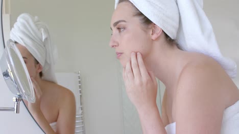 Caucasian-woman-with-towel-on-head-touching-her-face-in-front-of-mirror-in-bathroom-in-slow-motion